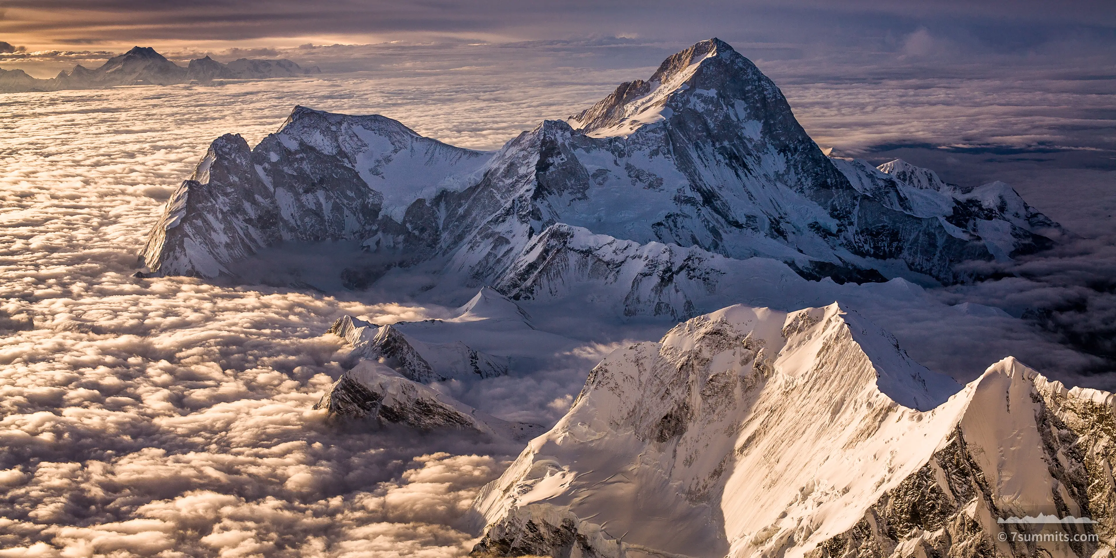 Snow-covered summit of Makalu rising above a level sea of cloud, lit from the side by low sun, under a dark banded sky.
