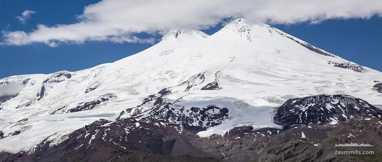 Snow-capped twin peaks of Mount Elbrus seen from Mount Cheget under blue sky
