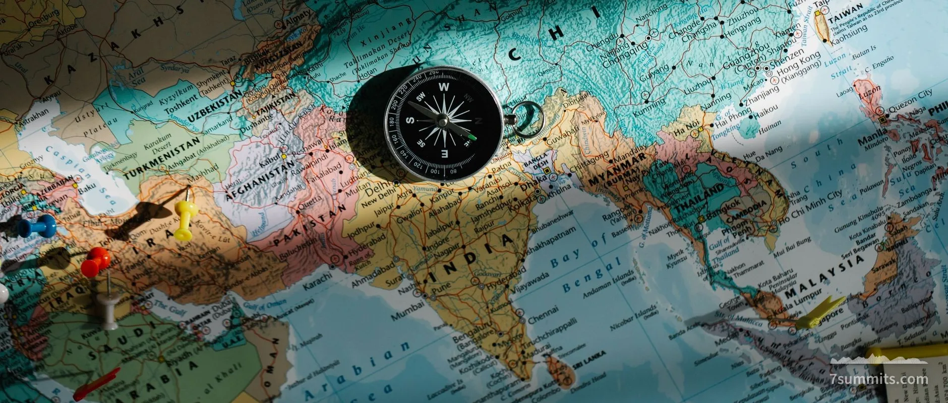 roadmap — A compass placed on a detailed world map with colored push pins.