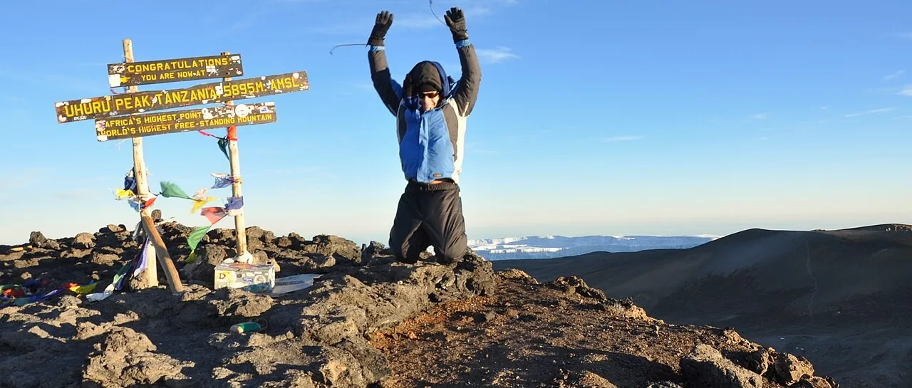 A climber jumps for joy at the Uhuru Peak summit sign on Mount Kilimanjaro, Tanzania.