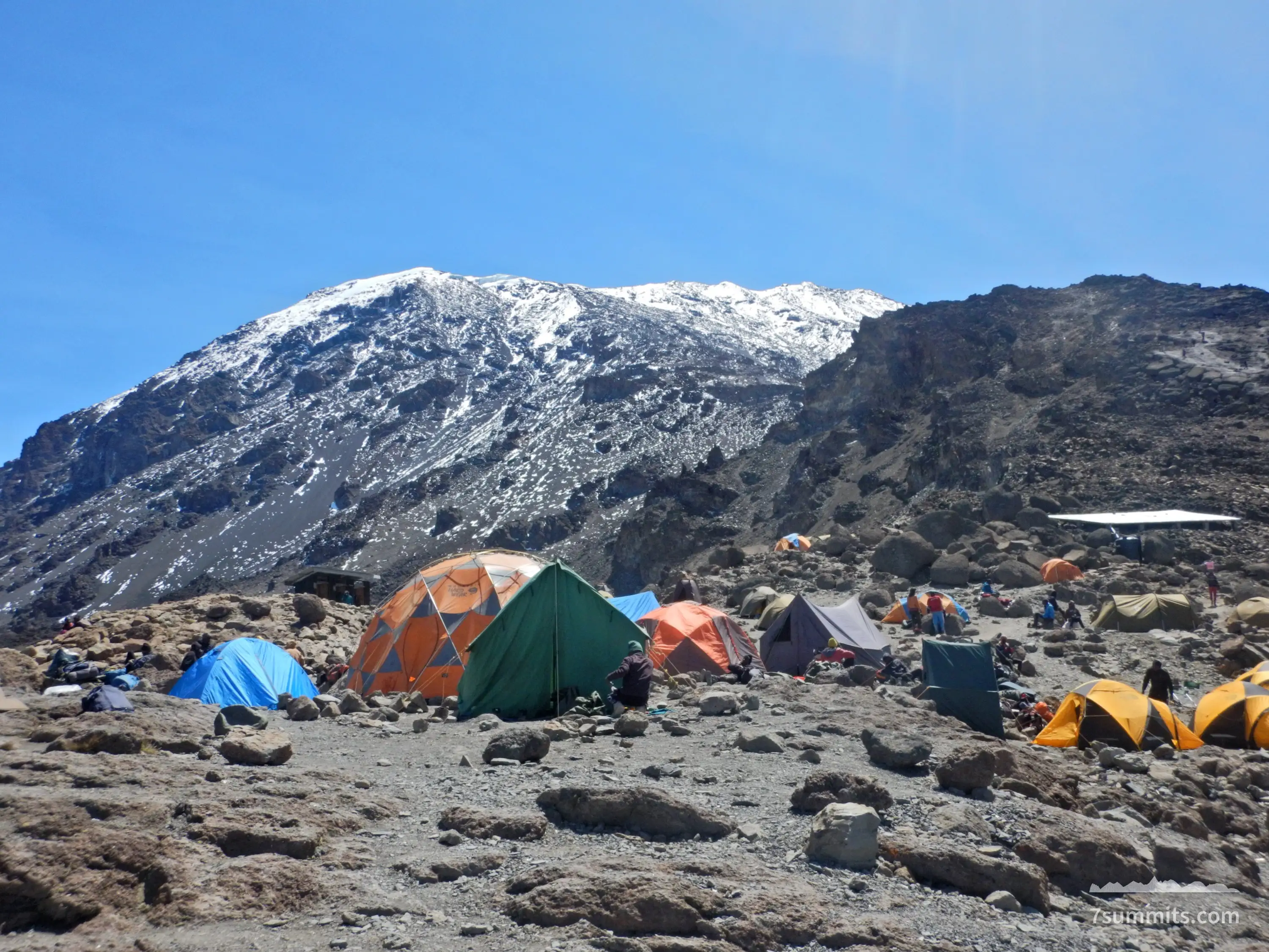 Colorful tents clustered on rocky ground below snow-capped summit at Barafu Camp