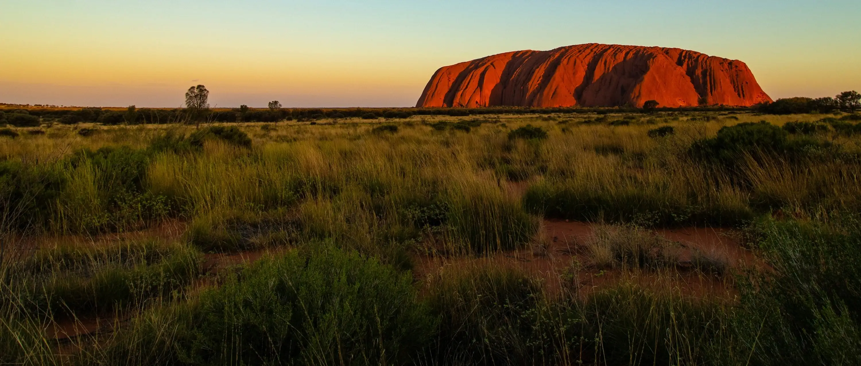 Australia — Uluru glowing in the low sun above a vast desert landscape in Australia